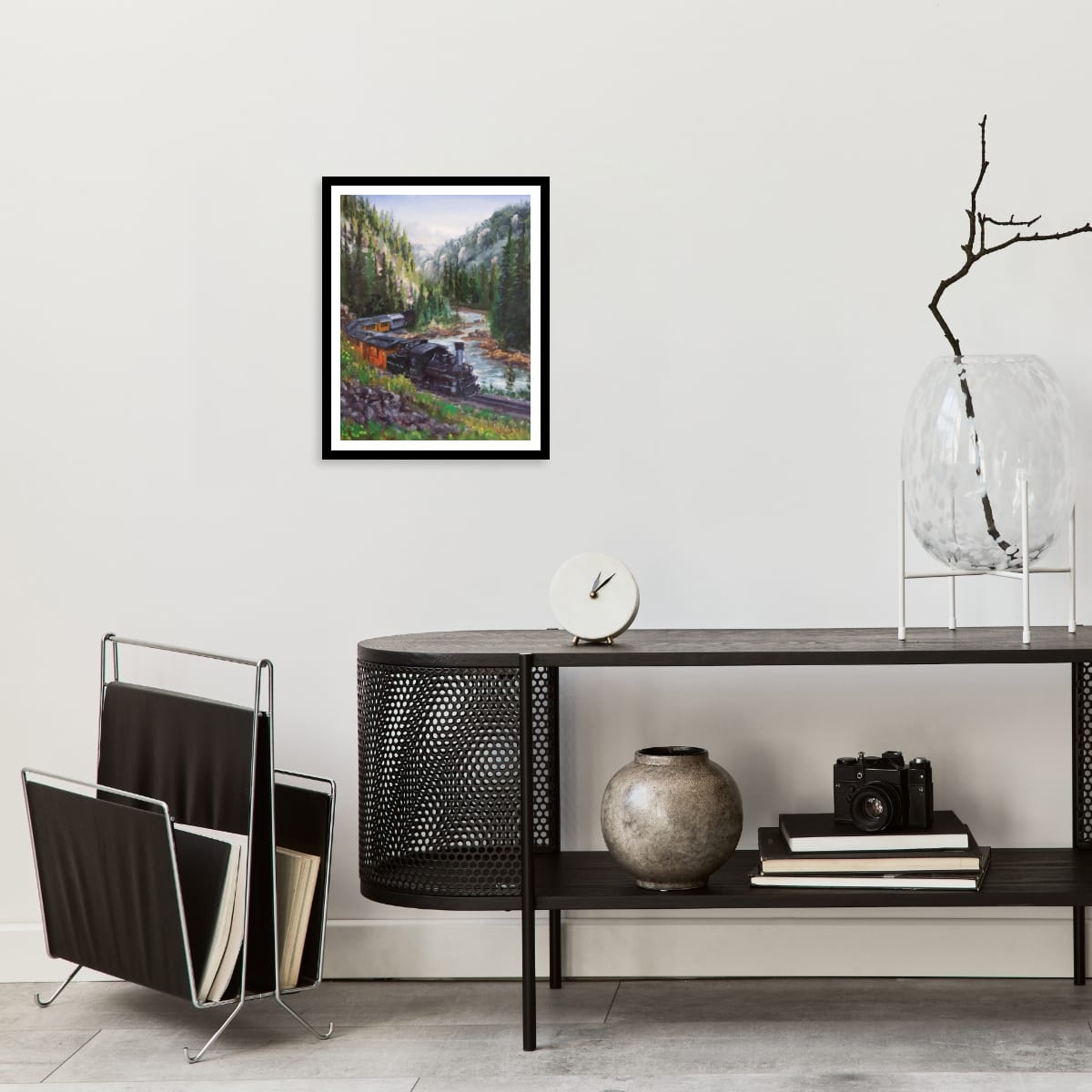 Modern interior with a black console table, magazine rack, and framed original oil painting of the Durango and Silverton in a mountain setting 
